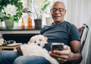 Henkilöllä sylissään koira ja hän pitelee kännykkää kaukana ikään kuin nähdäkseen paremmin.